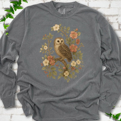 Pepper long sleeve T-shirt flat lay with a botanical illustration of a brown owl perched on a branch, framed by wild roses, cream blossoms, rosehips and olive-green leaves, on white brick with ivy.