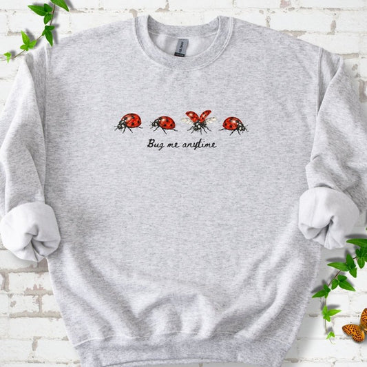 Ash classic sweatshirt laid flat, showing four red and black ladybugs above "Bug me anytime" lettering.