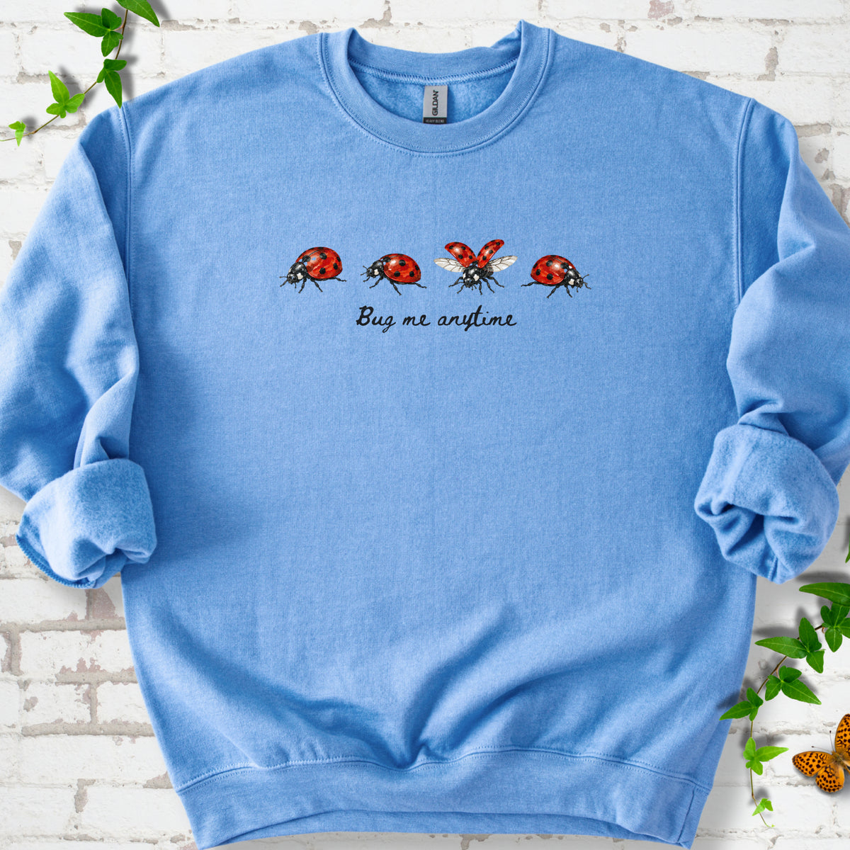 Carolina Blue classic sweatshirt laid flat, showing four red and black ladybugs above "Bug me anytime" lettering.