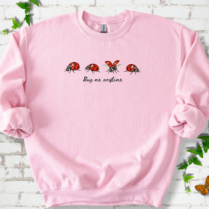 Light Pink classic sweatshirt laid flat, showing four red and black ladybugs above "Bug me anytime" lettering.