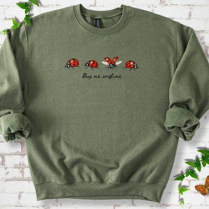 Military Green classic sweatshirt laid flat, showing four red and black ladybugs above "Bug me anytime" lettering.