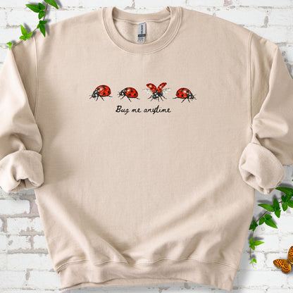 Sand classic sweatshirt laid flat, showing four red and black ladybugs above "Bug me anytime" lettering.