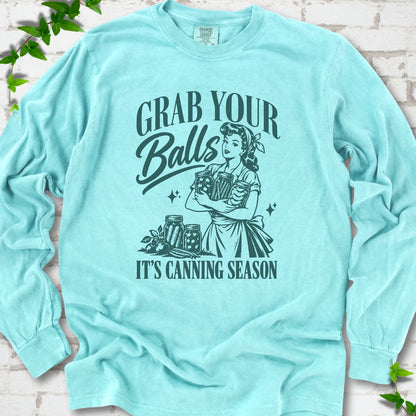 Chalky Mint long sleeve T-shirt flat lay with a deep teal retro illustration of a 1950s-style woman in a headscarf and apron hugging three filled canning jars, more jars and vegetables at her feet, with "Grab your" above, "Balls" in script and "It's canning season" below, on white brick with ivy.