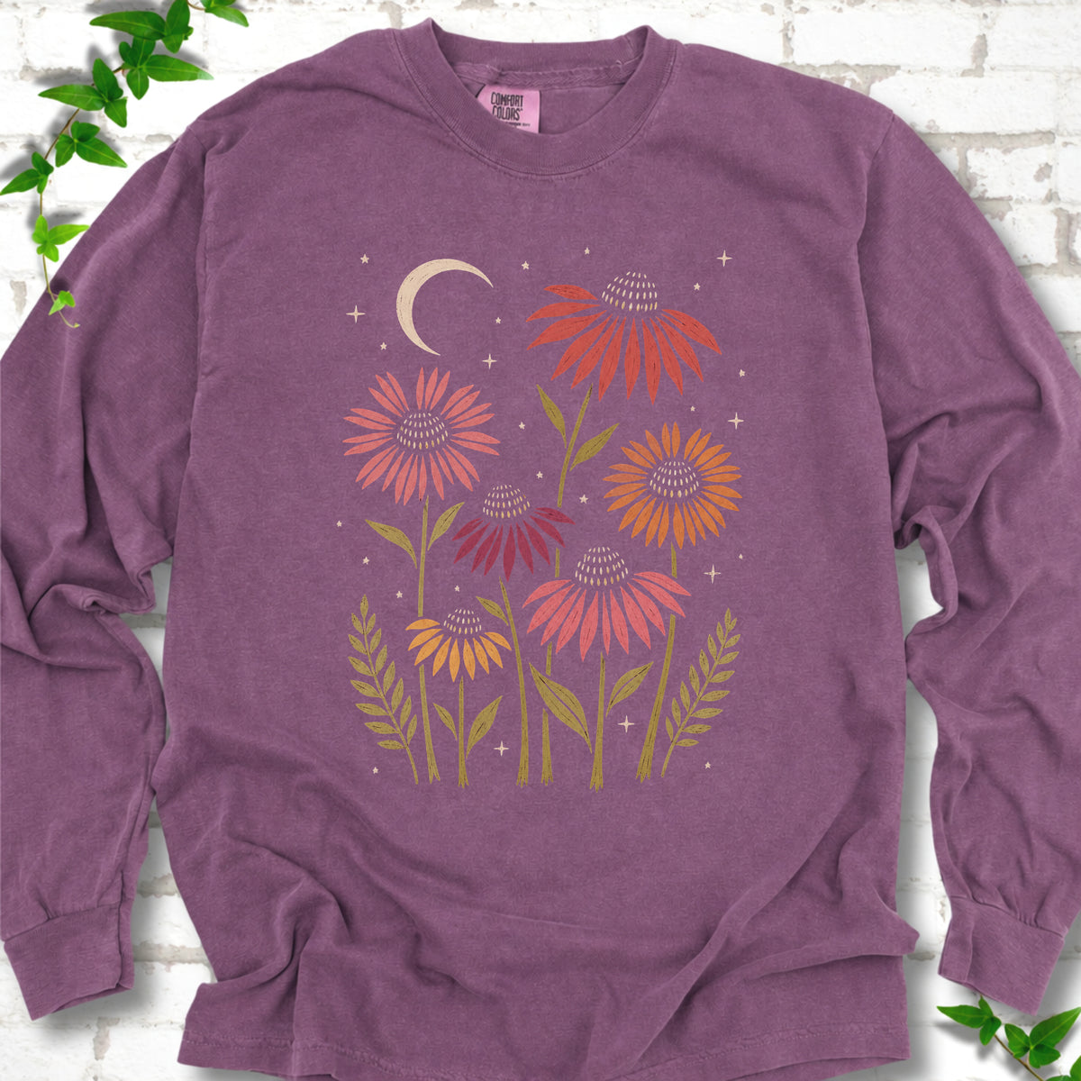 Berry long sleeve tee laid flat, showing warm-toned coneflowers with green leaves, a cream crescent moon and small stars.