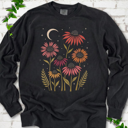 Black long sleeve tee laid flat, showing warm-toned coneflowers with green leaves, a cream crescent moon and small stars.