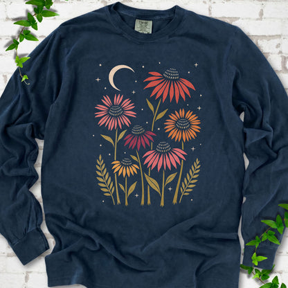 Midnight long sleeve tee laid flat, showing warm-toned coneflowers with green leaves, a cream crescent moon and small stars.