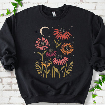 Black classic sweatshirt laid flat, showing warm-toned coneflowers with green leaves, a cream crescent moon and small stars.