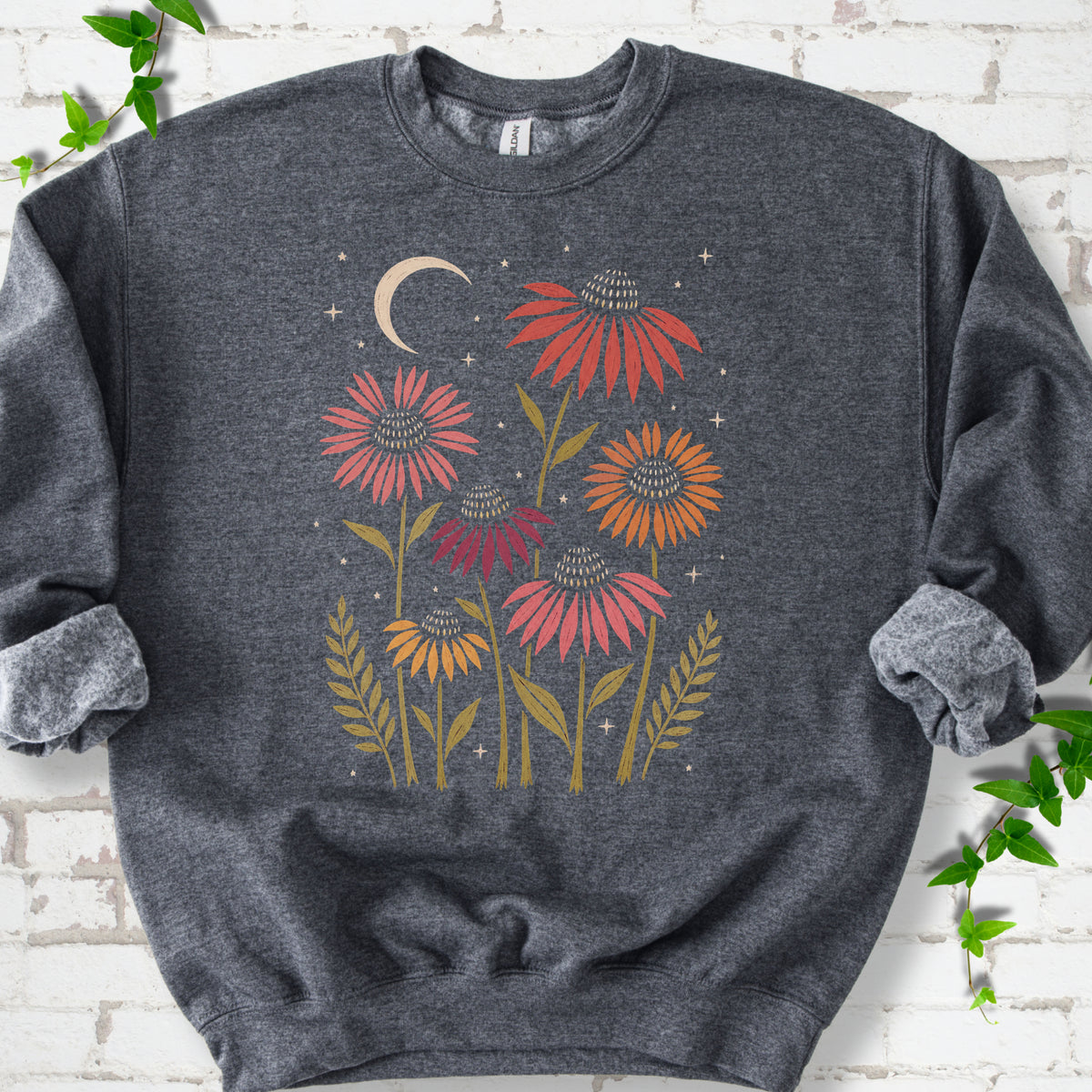 Dark Heather classic sweatshirt laid flat, showing warm-toned coneflowers with green leaves, a cream crescent moon and small stars.