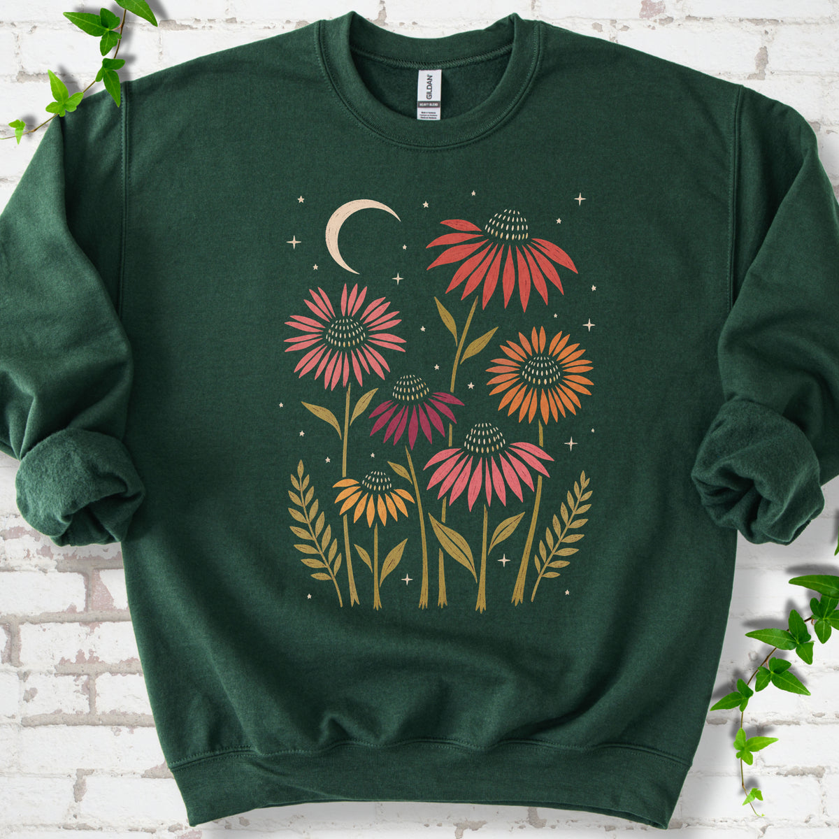 Forest Green classic sweatshirt laid flat, showing warm-toned coneflowers with green leaves, a cream crescent moon and small stars.