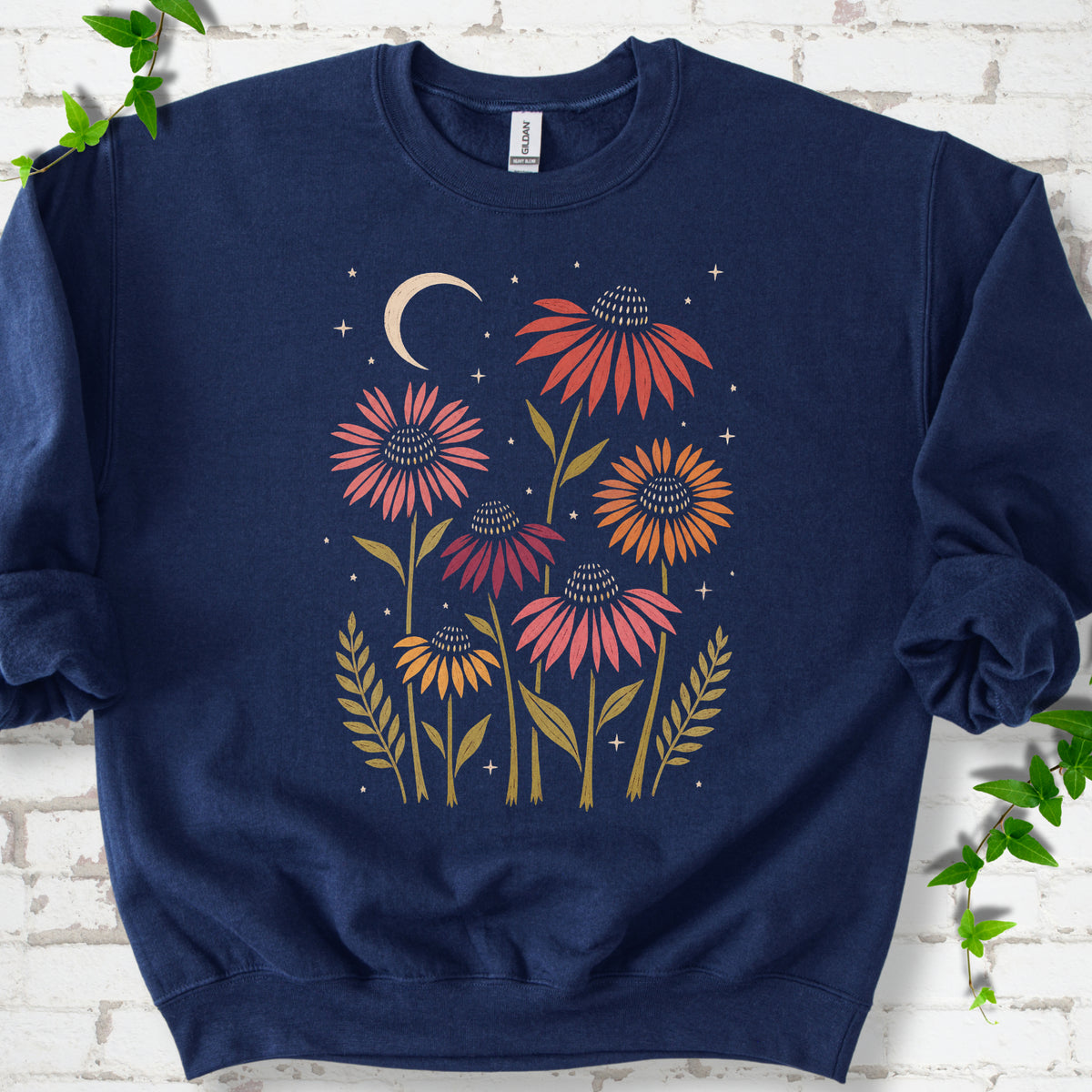 Navy classic sweatshirt laid flat, showing warm-toned coneflowers with green leaves, a cream crescent moon and small stars.