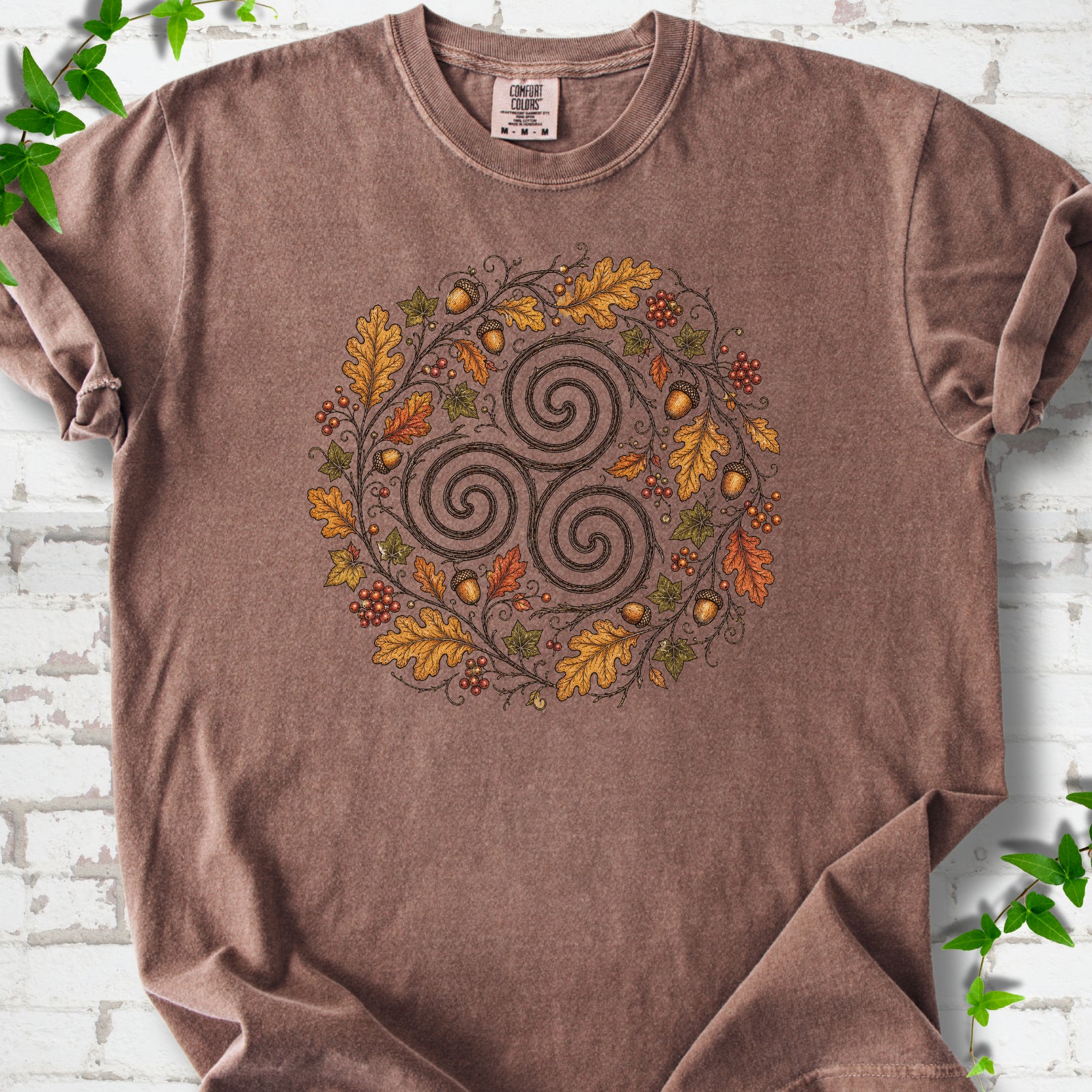 Espresso Comfort Colors® T-shirt flat lay with a Celtic-inspired triskele and autumn oak wreath design.