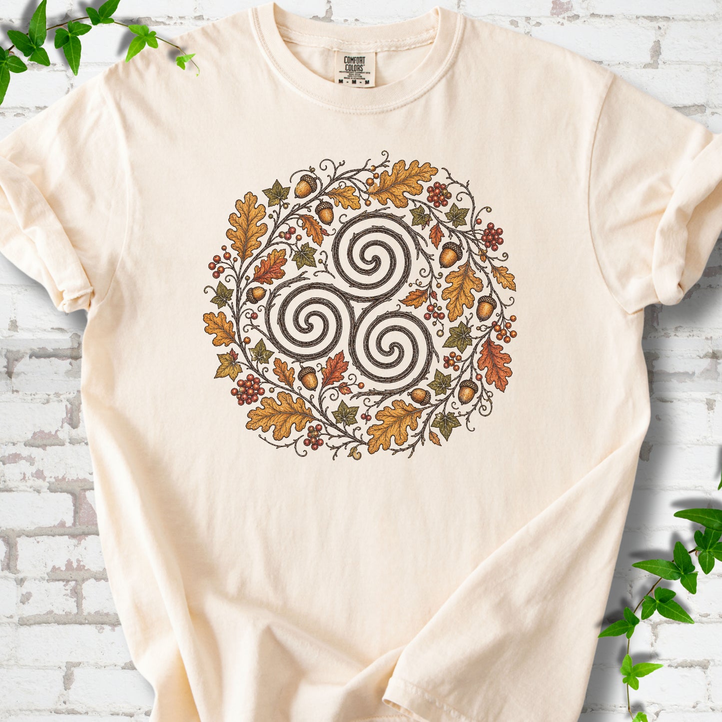Ivory Comfort Colors® T-shirt flat lay with a Celtic-inspired triskele and autumn oak wreath design.