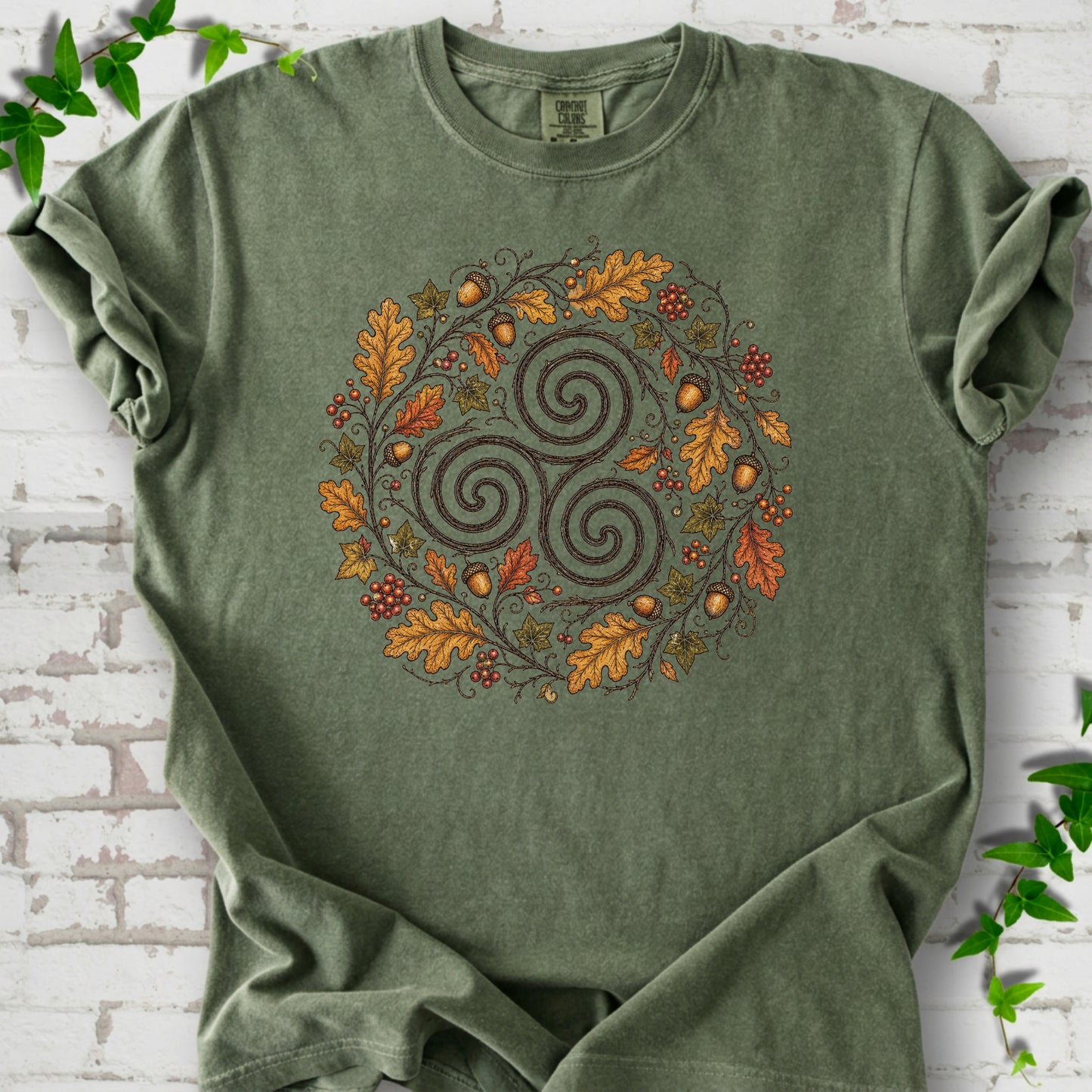 Moss Comfort Colors® T-shirt flat lay with a Celtic-inspired triskele and autumn oak wreath design.