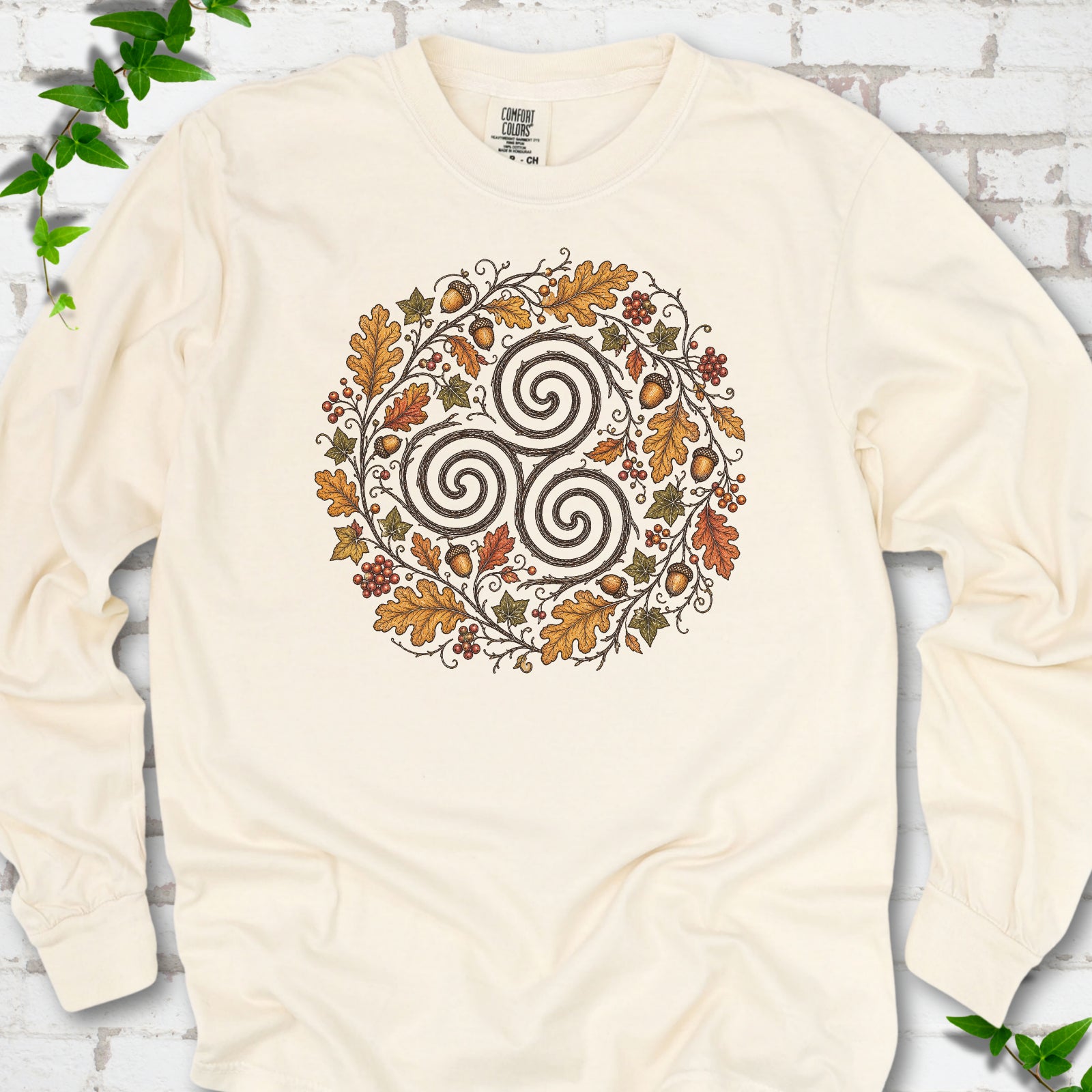 Ivory Comfort Colors® long sleeve T-shirt flat lay with a Celtic-inspired triskele and autumn oak wreath design.