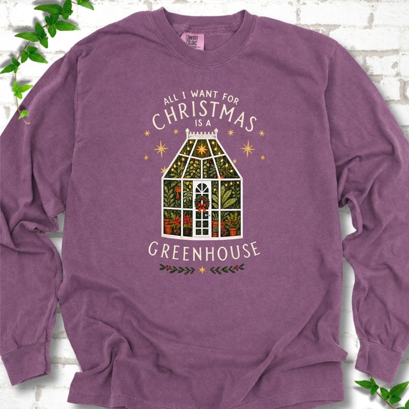 Berry long sleeve T-shirt laid flat, featuring a plant-filled glass greenhouse with a red bow, gold stars and the slogan 'All I want for Christmas is a greenhouse'.