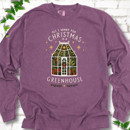 Berry long sleeve T-shirt laid flat, featuring a plant-filled glass greenhouse with a red bow, gold stars and the slogan 'All I want for Christmas is a greenhouse'.