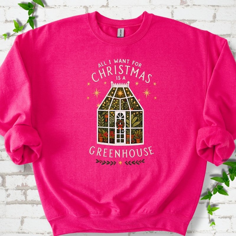 Heliconia sweatshirt laid flat, featuring a plant-filled glass greenhouse with a red bow, gold stars and the slogan 'All I want for Christmas is a greenhouse'.