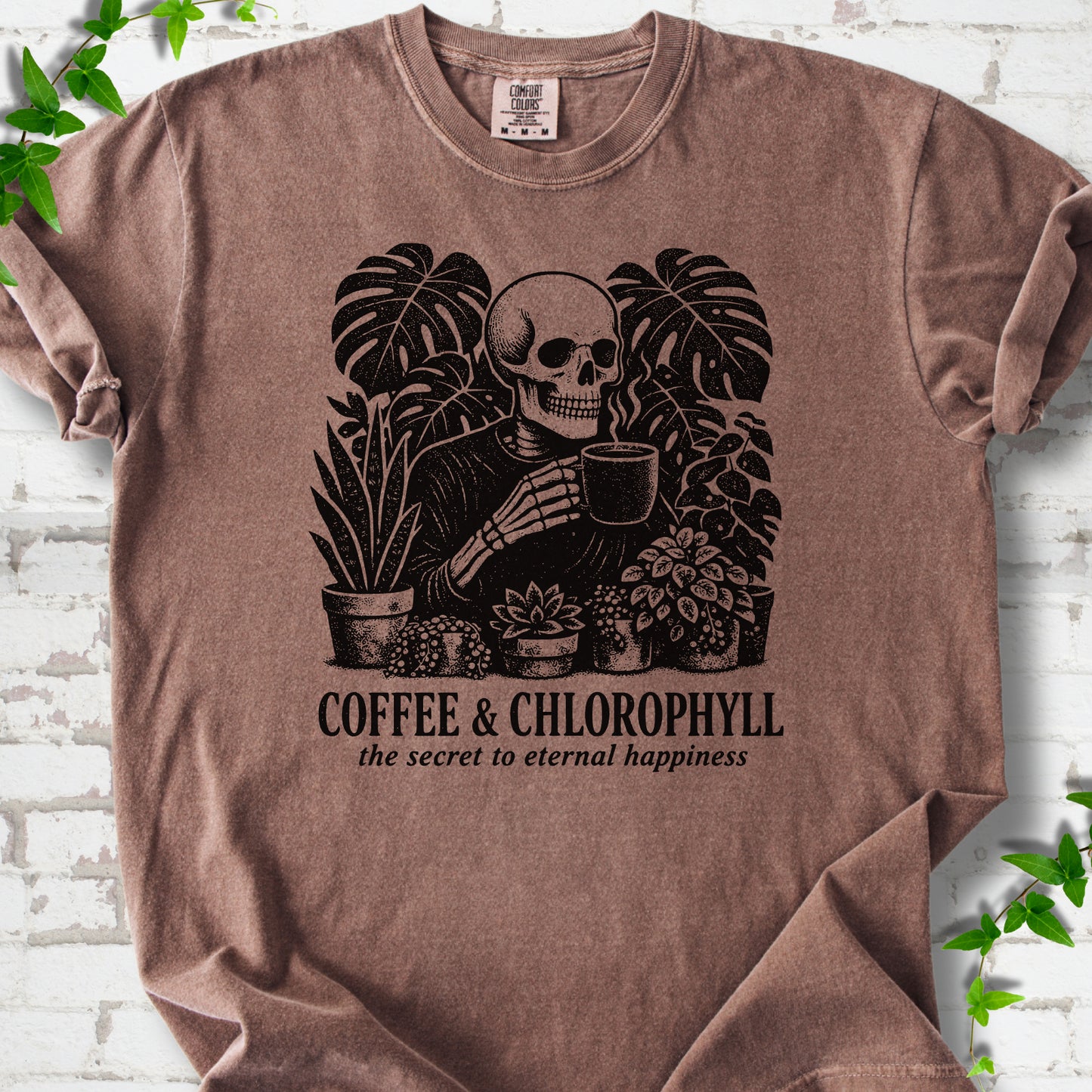 Espresso Comfort Colors® short sleeve T-shirt flat lay featuring a distressed skeleton drinking coffee among houseplants