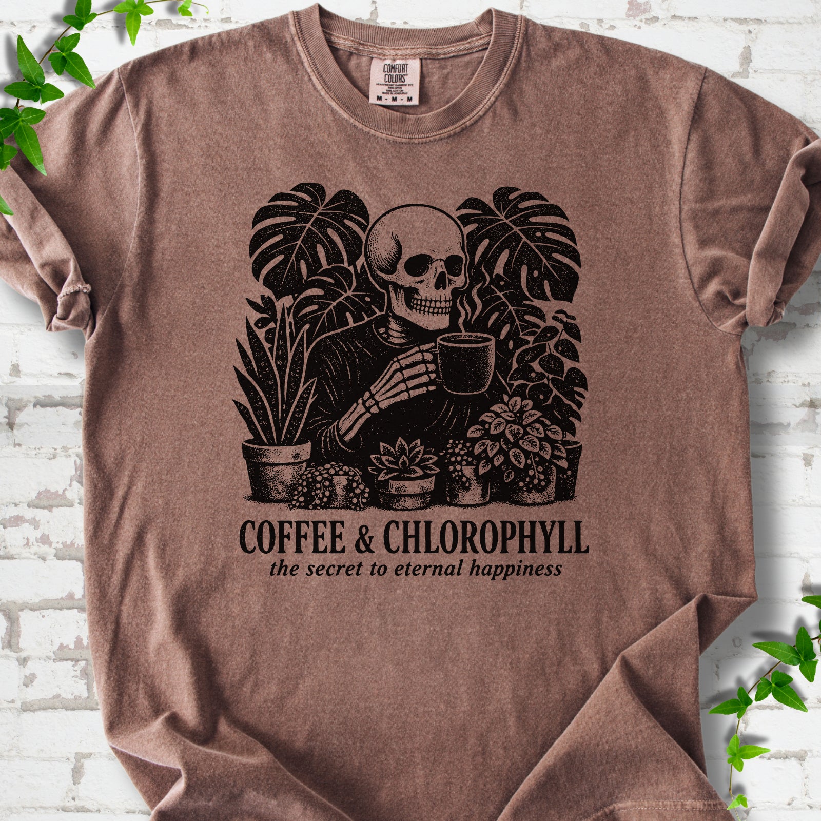 Espresso Comfort Colors® short sleeve T-shirt flat lay featuring a distressed skeleton drinking coffee among houseplants