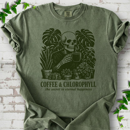 Moss Comfort Colors® short sleeve T-shirt flat lay featuring a distressed skeleton drinking coffee among houseplants