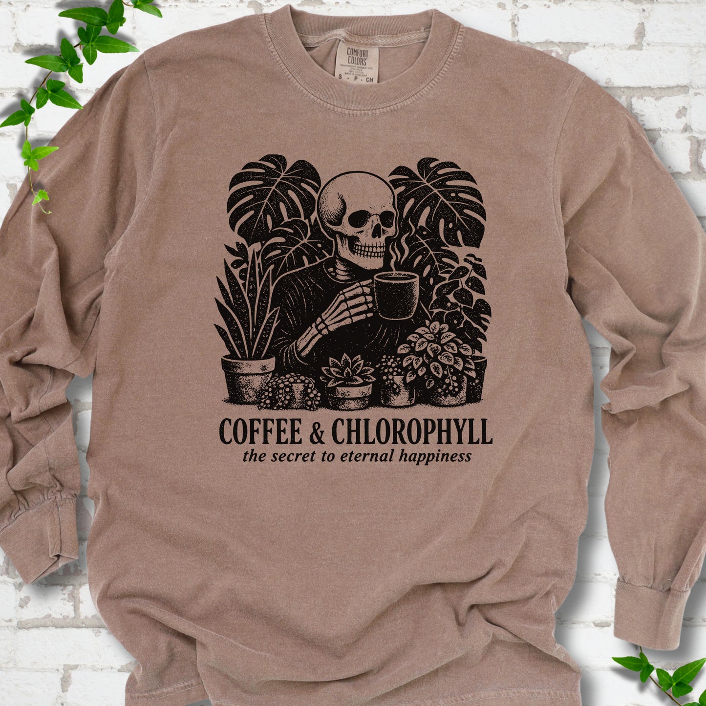 Espresso Comfort Colors® long sleeve T-shirt flat lay featuring a distressed skeleton drinking coffee among houseplants