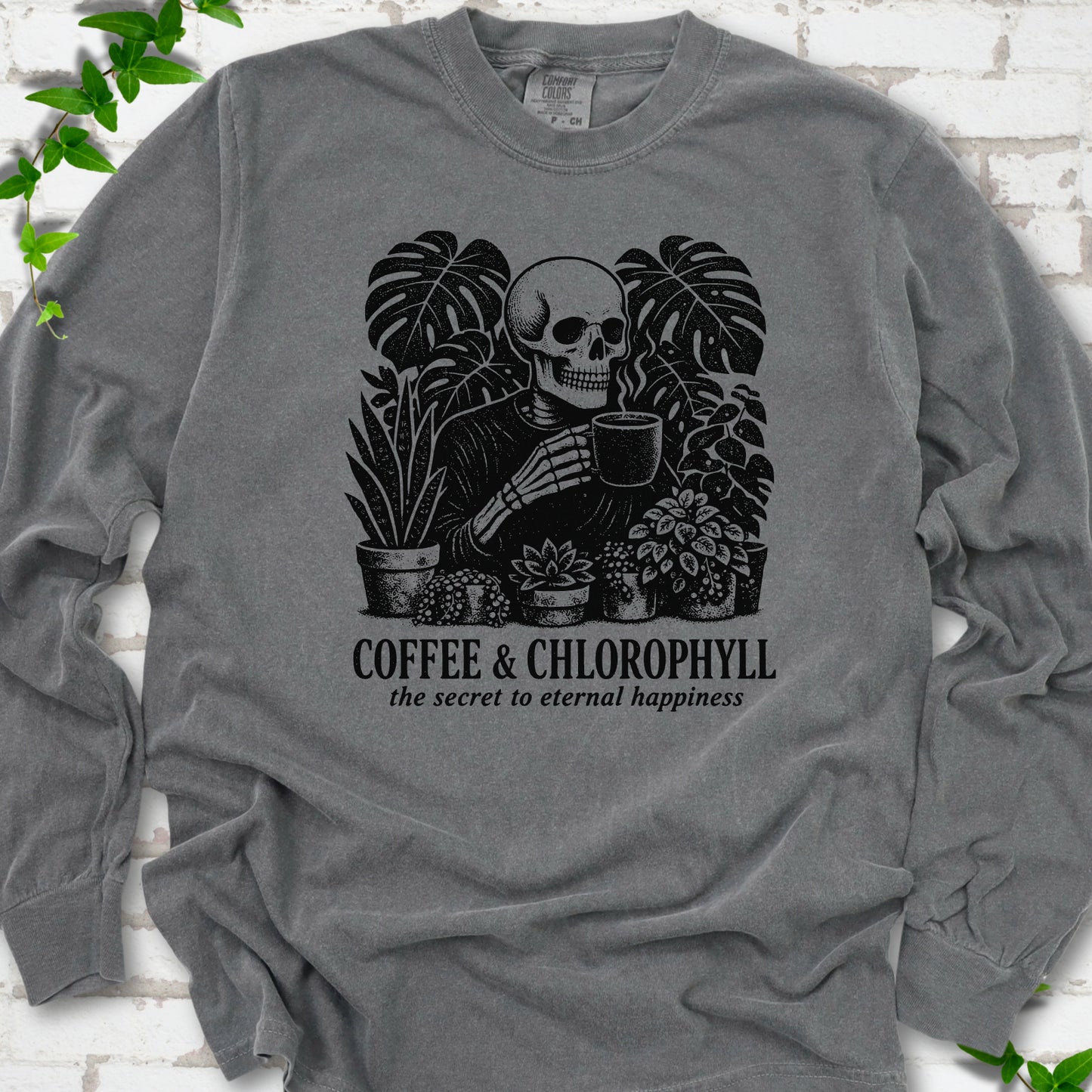 Pepper Comfort Colors® long sleeve T-shirt flat lay featuring a distressed skeleton drinking coffee among houseplants