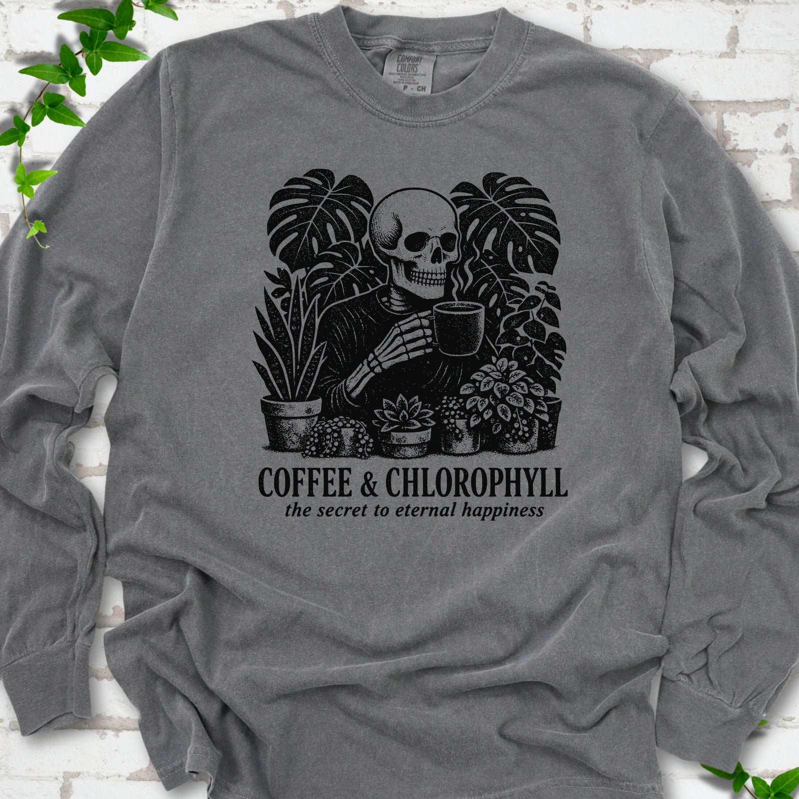 Pepper Comfort Colors® long sleeve T-shirt flat lay featuring a distressed skeleton drinking coffee among houseplants