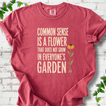 Crimson Comfort Colors® short sleeve T-shirt flat lay with cream text reading "Common sense is a flower that does not grow in everyone's garden" beside a yellow flower