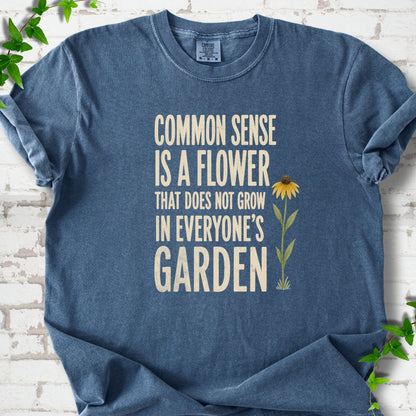 Denim Comfort Colors® short sleeve T-shirt flat lay with cream text reading "Common sense is a flower that does not grow in everyone's garden" beside a yellow flower