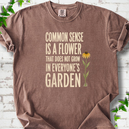 Espresso Comfort Colors® short sleeve T-shirt flat lay with cream text reading "Common sense is a flower that does not grow in everyone's garden" beside a yellow flower