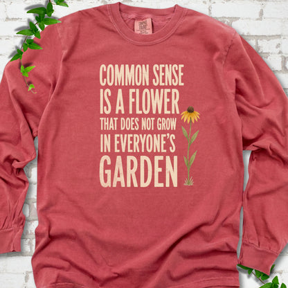 Crimson Comfort Colors® long sleeve T-shirt flat lay with cream text reading "Common sense is a flower that does not grow in everyone's garden" beside a yellow flower