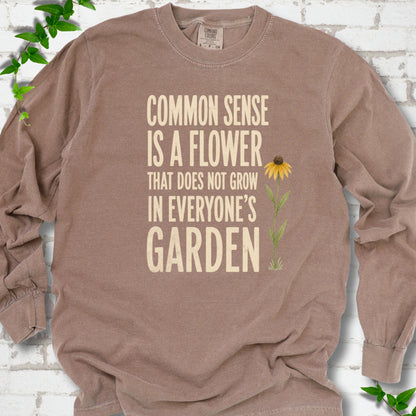 Espresso Comfort Colors® long sleeve T-shirt flat lay with cream text reading "Common sense is a flower that does not grow in everyone's garden" beside a yellow flower