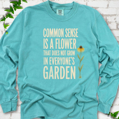 Seafoam Comfort Colors® long sleeve T-shirt flat lay with cream text reading "Common sense is a flower that does not grow in everyone's garden" beside a yellow flower