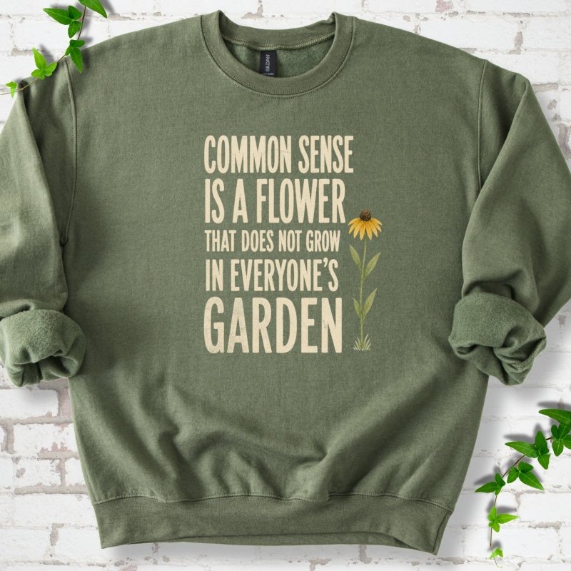 Military Green Gildan® 18000 crewneck sweatshirt flat lay with cream text reading ‘Common sense is a flower that does not grow in everyone's garden’ and a yellow flower