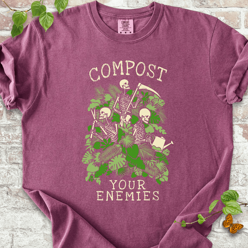 Compost Your Enemies Skeleton T-Shirt on Comfort Colors™ Berry – features a garden-themed skeleton trio hiding in a mass of tropical leaves and bold green foliage