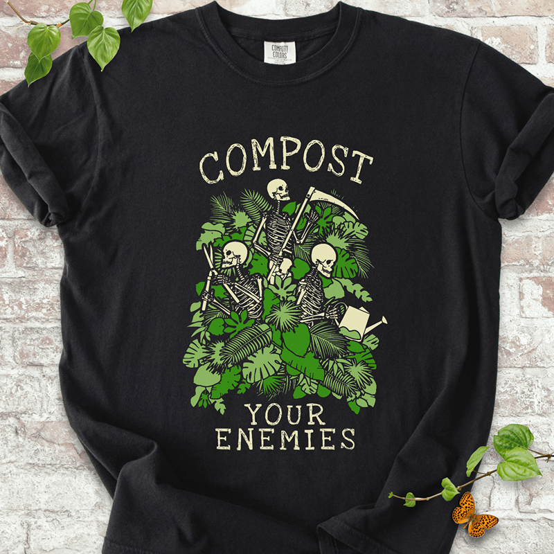Compost Your Enemies Skeleton T-Shirt on Comfort Colors™ Black – shows a skeleton trio with garden tools peeking out from behind dense green jungle leaves