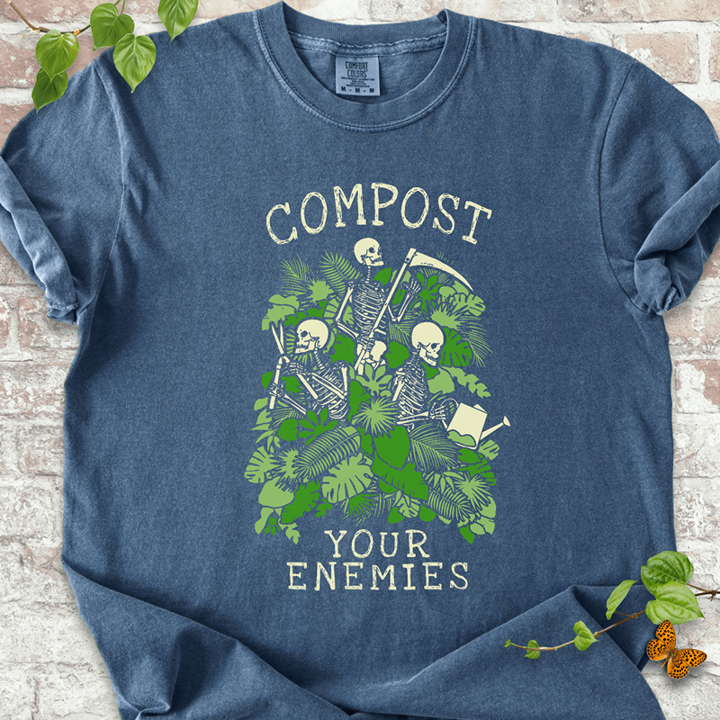 Compost Your Enemies Skeleton T-Shirt on Comfort Colors™ Denim – shows three skeletons with gardening tools surrounded by dense green foliage and jungle-style leaves