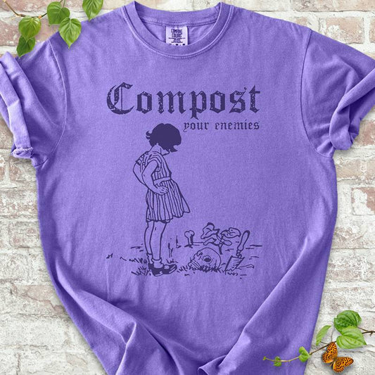 Compost Your Enemies T-shirt on Comfort Colors™ Violet – features gothic-style text and a vintage illustration of a little girl staring down at a buried skeleton with mushrooms and a shovel