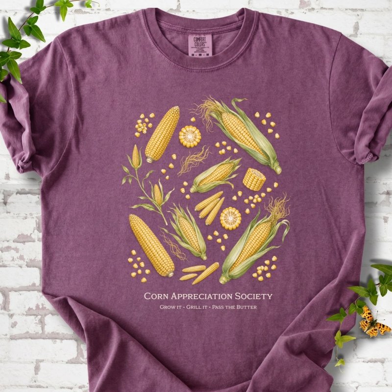 Berry Comfort Colors® short sleeve T-shirt flat lay featuring ears, kernels and corn plants with text "Corn Appreciation Society" and "Grow it, grill it, pass the butter"