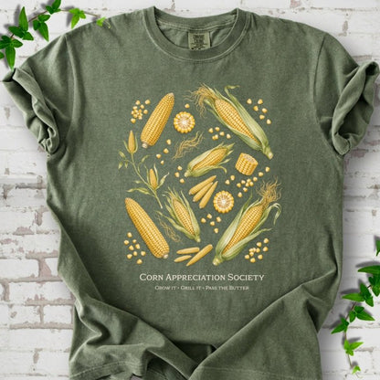Moss Comfort Colors® short sleeve T-shirt flat lay featuring ears, kernels and corn plants with text "Corn Appreciation Society" and "Grow it, grill it, pass the butter"
