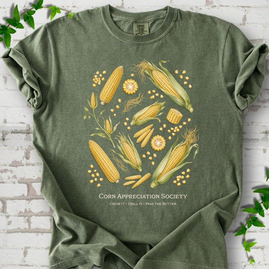 Moss Comfort Colors® short sleeve T-shirt flat lay featuring ears, kernels and corn plants with text "Corn Appreciation Society" and "Grow it, grill it, pass the butter"