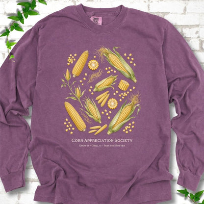 Berry Comfort Colors® long sleeve T-shirt flat lay featuring ears, kernels and corn plants with text "Corn Appreciation Society" and "Grow it, grill it, pass the butter"