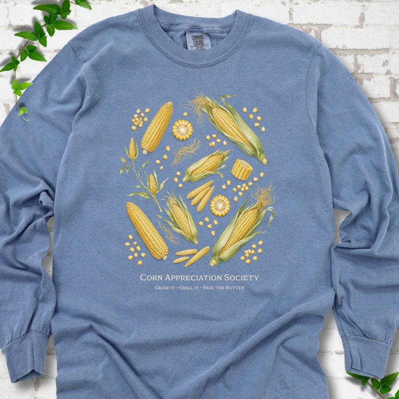 Blue Jean Comfort Colors® long sleeve T-shirt flat lay featuring ears, kernels and corn plants with text "Corn Appreciation Society" and "Grow it, grill it, pass the butter"