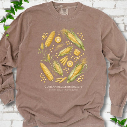 Espresso Comfort Colors® long sleeve T-shirt flat lay featuring ears, kernels and corn plants with text "Corn Appreciation Society" and "Grow it, grill it, pass the butter"