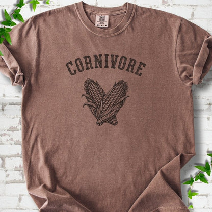Espresso Comfort Colors® short sleeve T-shirt flat lay featuring black line art of two sweet corn cobs beneath the word "Cornivore"