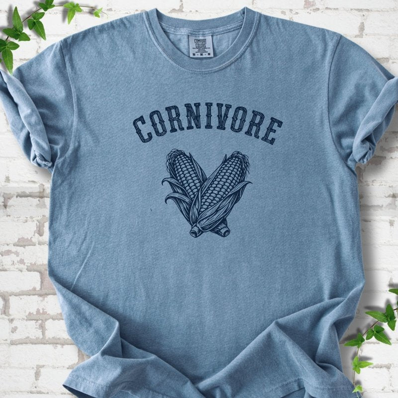 Blue Jean Comfort Colors® short sleeve T-shirt flat lay featuring black line art of two sweet corn cobs beneath the word "Cornivore"