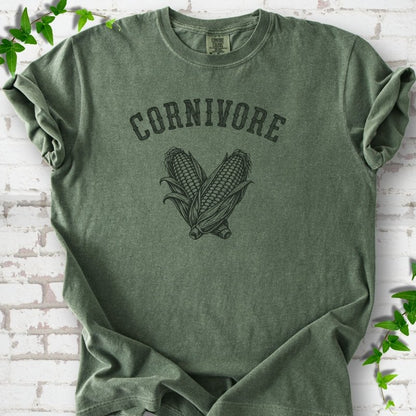 Moss Comfort Colors® short sleeve T-shirt flat lay featuring black line art of two sweet corn cobs beneath the word "Cornivore"