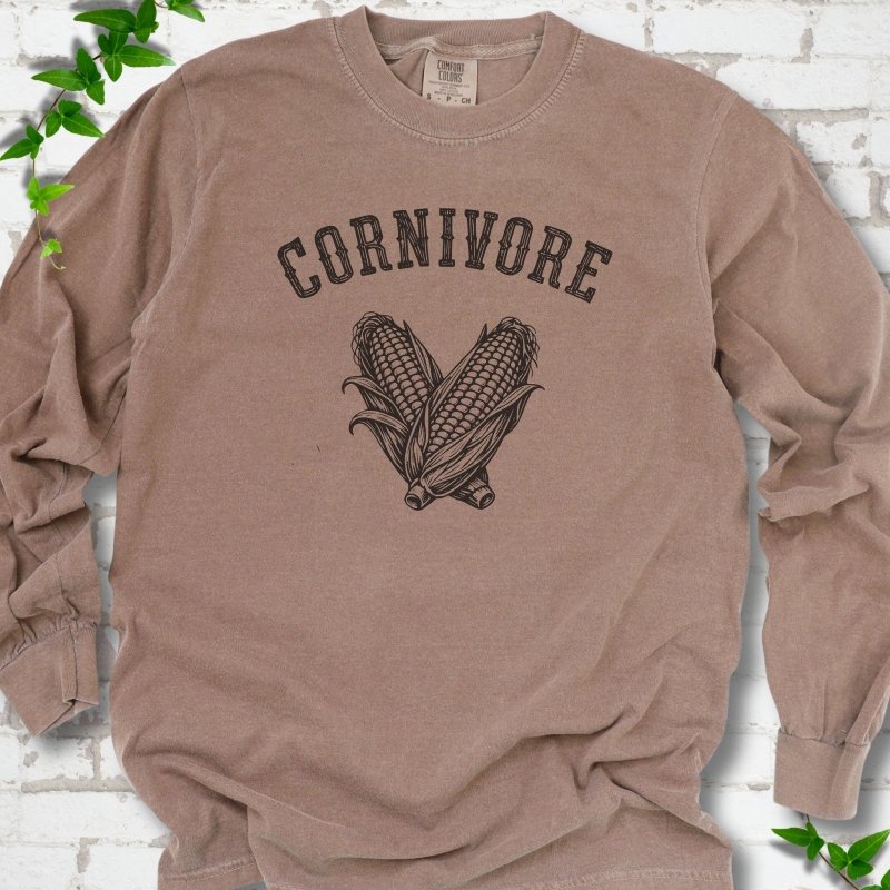 Espresso Comfort Colors® long sleeve T-shirt flat lay featuring black line art of two sweet corn cobs beneath the word "Cornivore"