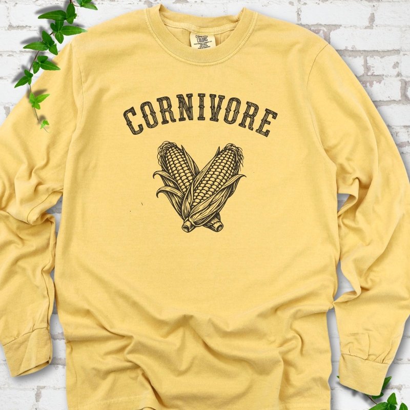 Mustard Comfort Colors® long sleeve T-shirt flat lay featuring black line art of two sweet corn cobs beneath the word "Cornivore"