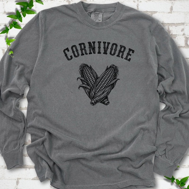 Pepper Comfort Colors® long sleeve T-shirt flat lay featuring black line art of two sweet corn cobs beneath the word "Cornivore"